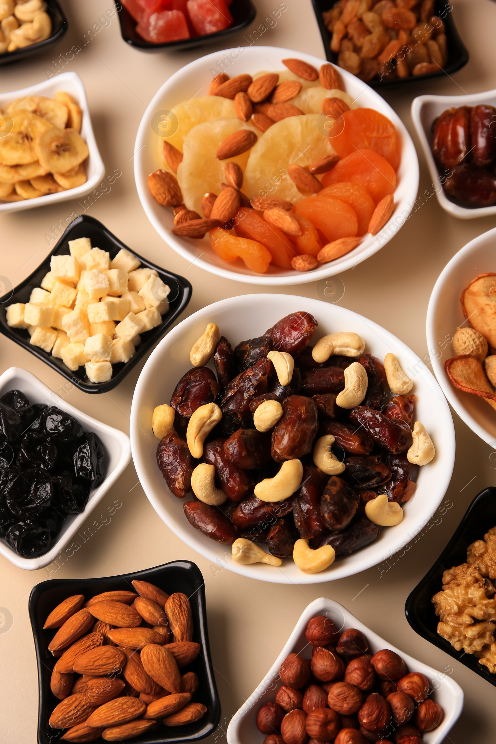 Photo of Bowls with dried fruits and nuts on beige background, above view