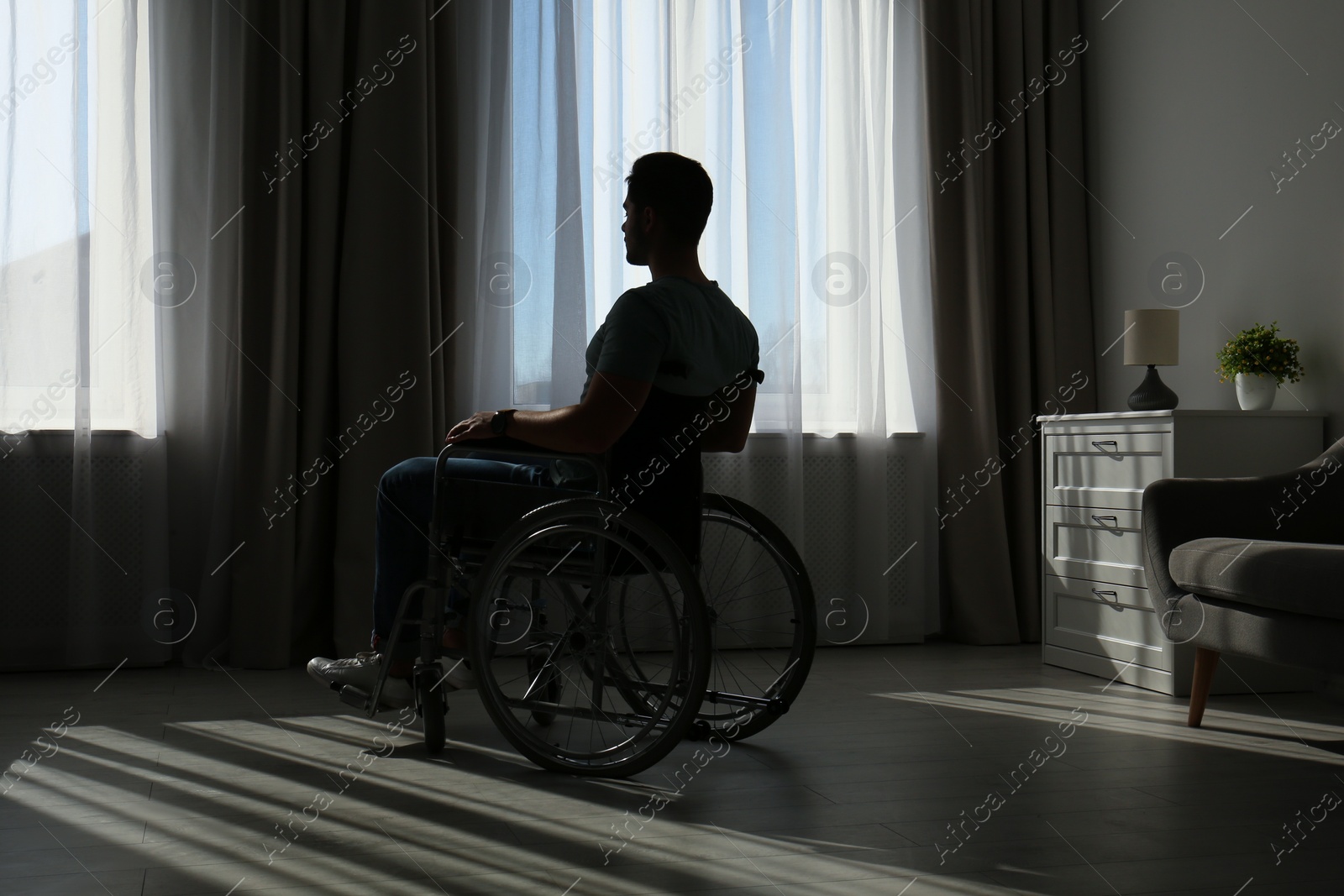 Photo of Young man sitting in wheelchair near window indoors