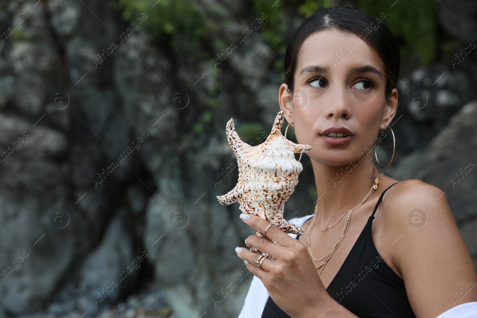 Photo of Beautiful young woman in stylish bikini holding seashell outdoors, space for text