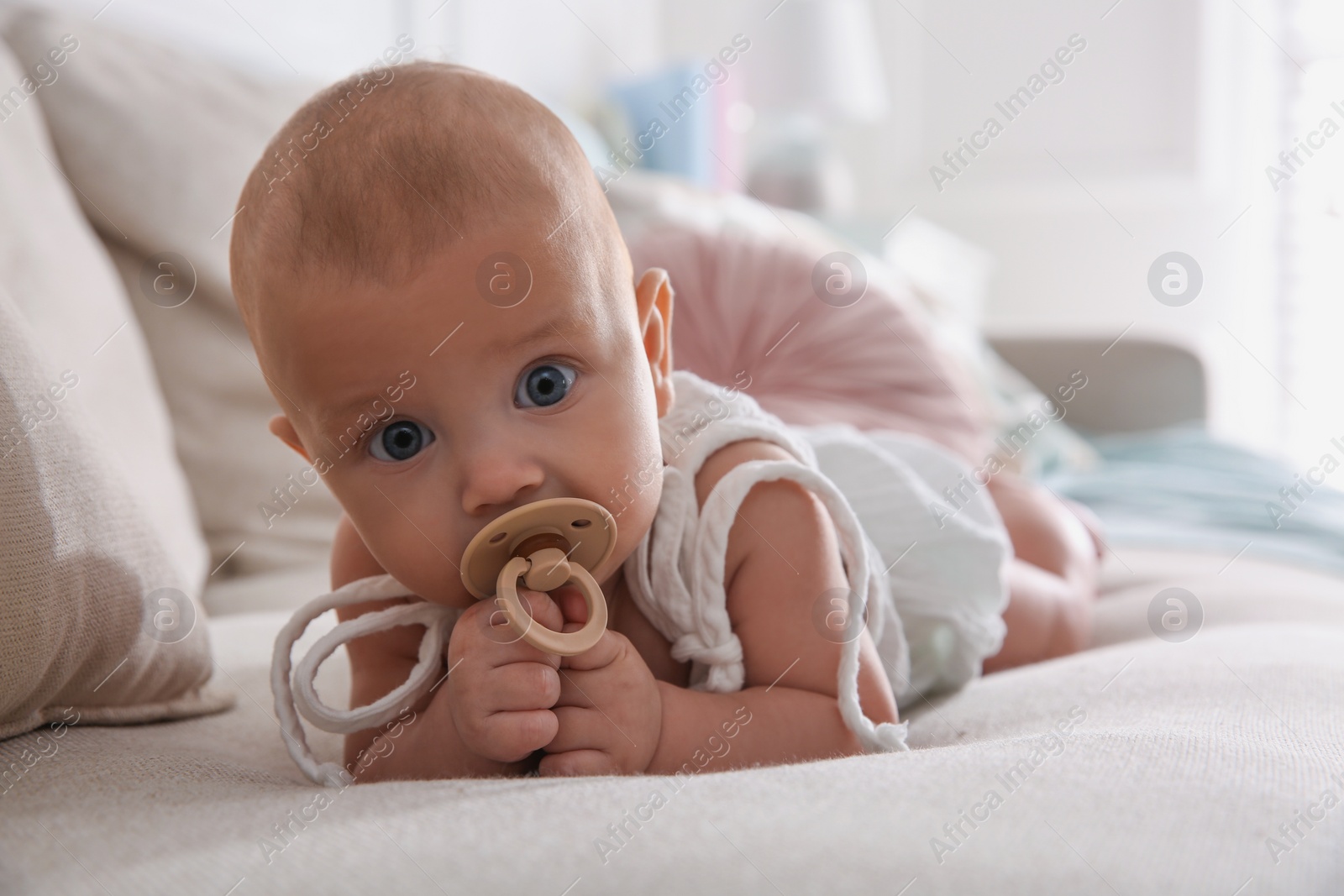 Photo of Cute little baby with pacifier on sofa at home