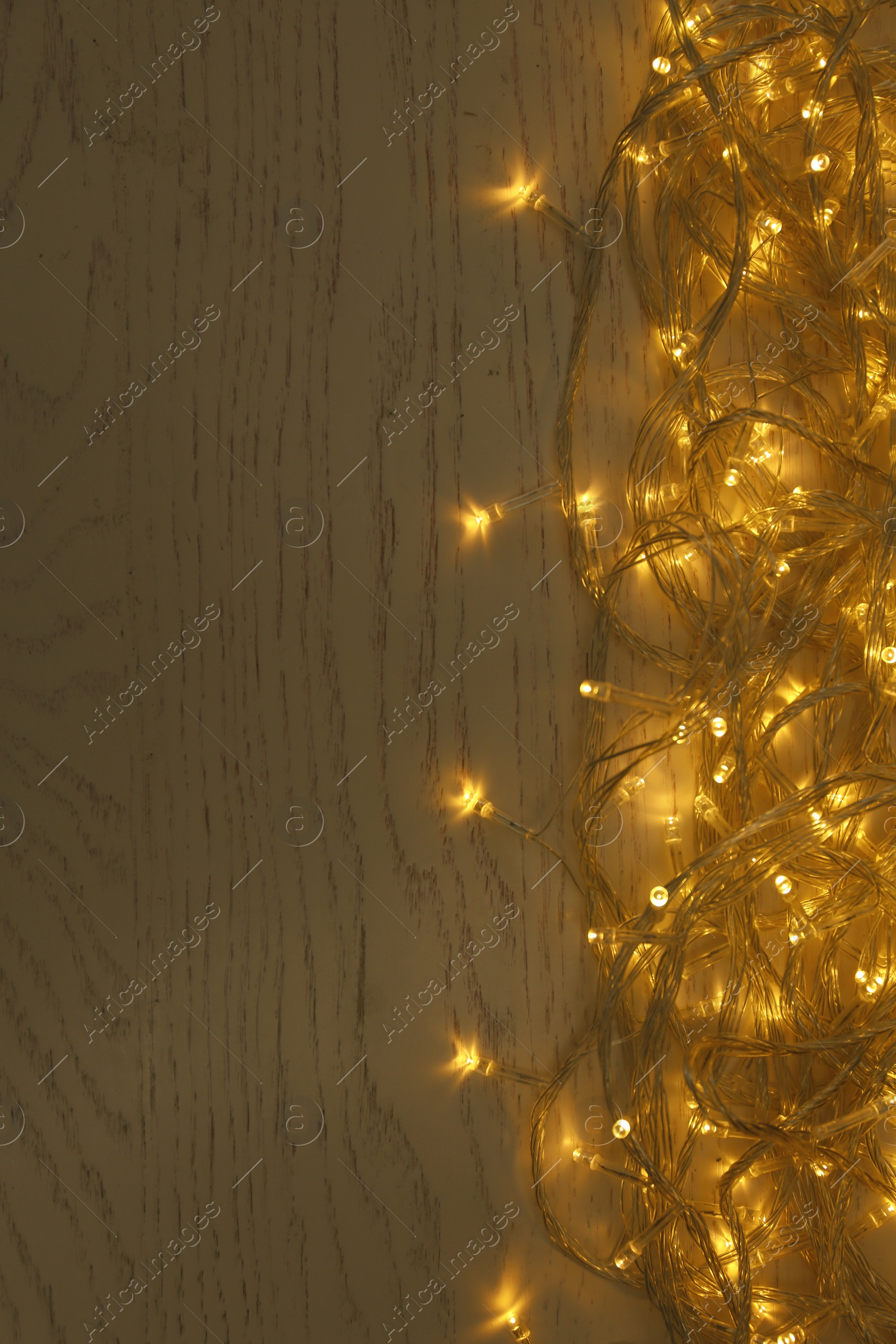 Photo of Glowing Christmas lights on white wooden background, top view. Space for text