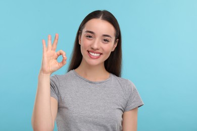 Photo of Young woman with clean teeth smiling and showing ok gesture on light blue background