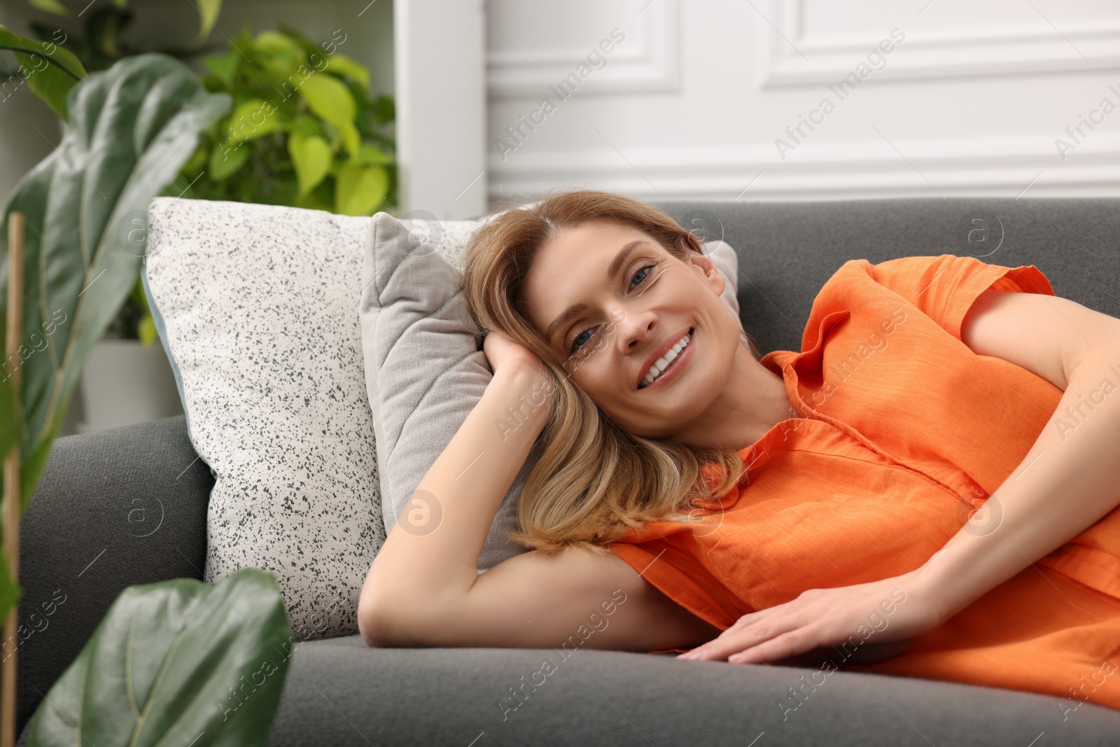 Photo of Woman relaxing on sofa in room with green houseplants