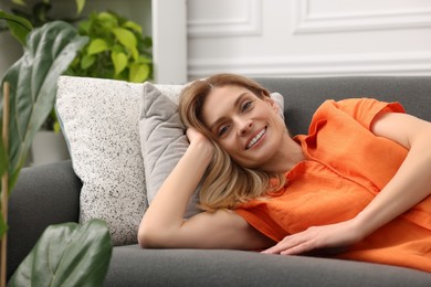 Woman relaxing on sofa in room with green houseplants