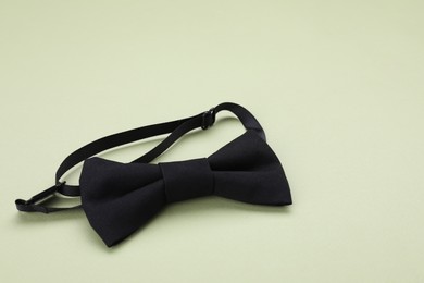 Photo of Stylish black bow tie on pale green background, space for text