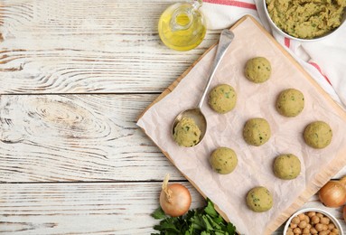 Raw falafel balls and ingredients on white wooden table, flat lay. Space for text