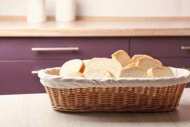 Wicker basket with slices of tasty fresh bread on wooden table in kitchen