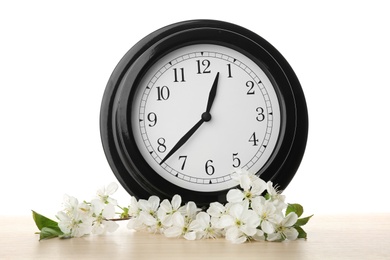 Photo of Big clock and branch with spring blossoms on table against white background. Time change concept