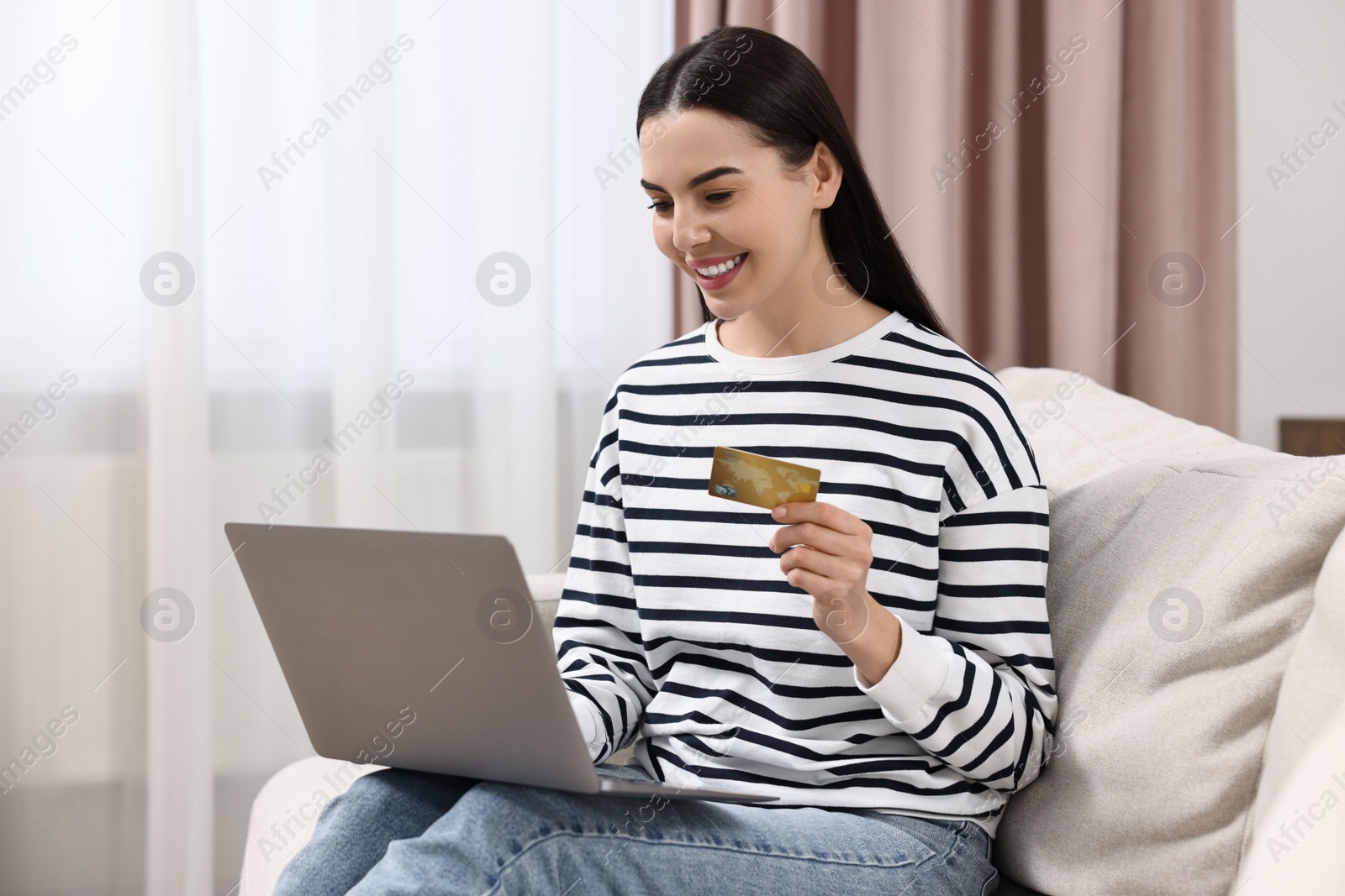 Photo of Happy young woman with credit card and laptop shopping online at home