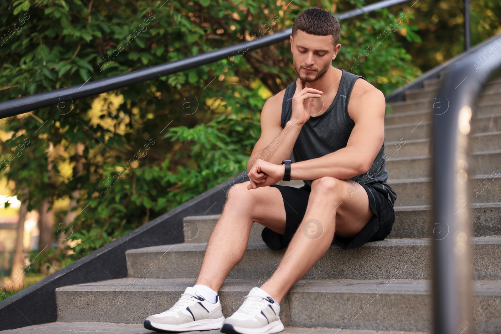 Photo of Attractive serious man checking pulse after training on stairs in park