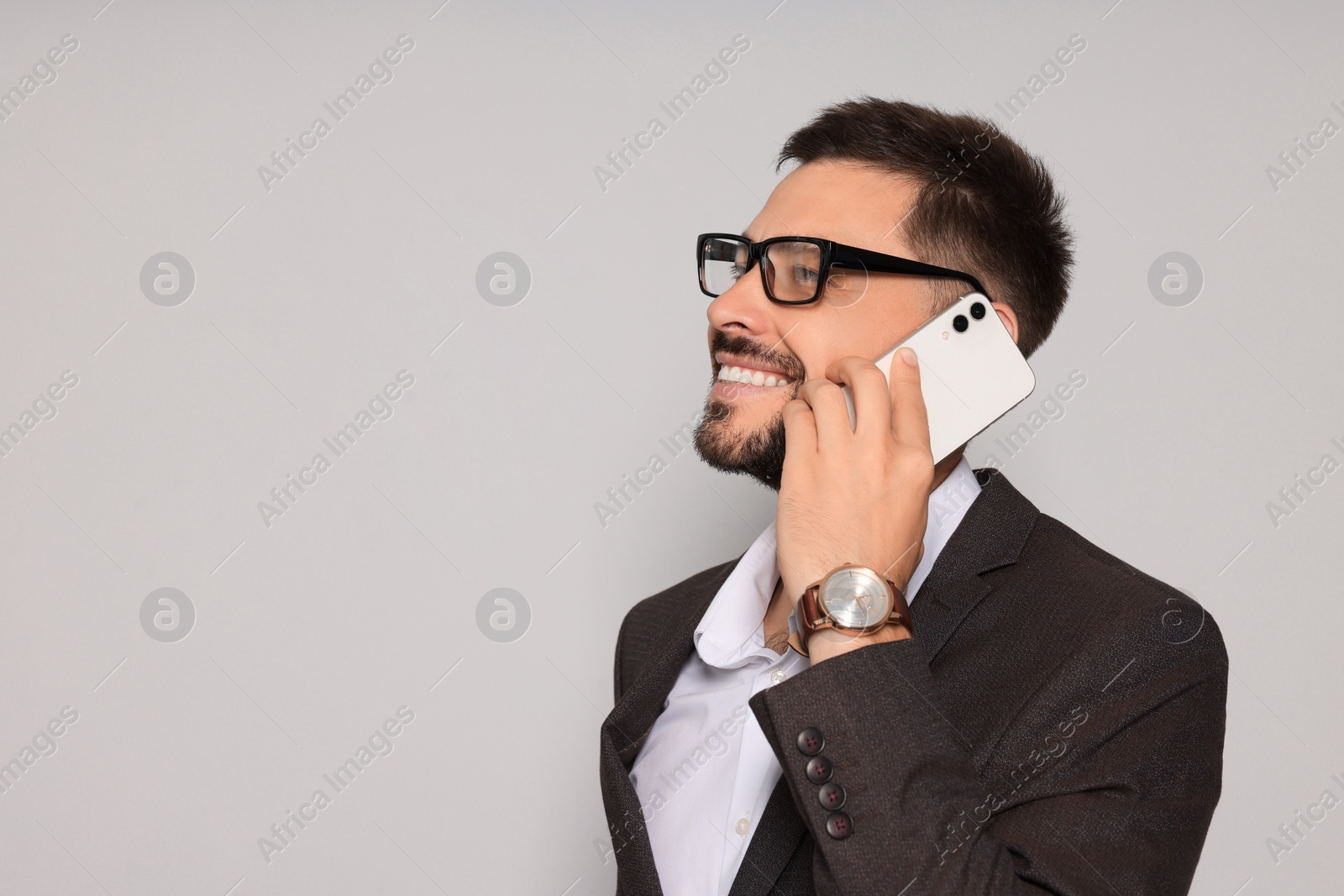 Photo of Handsome man in suit talking on smartphone against light grey background. Space for text