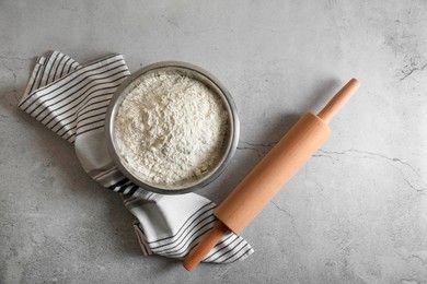 Photo of Flour in bowl, rolling pin and napkin on grey table, top view