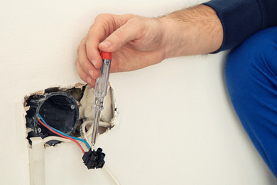 Image of Electrician with neon-lamp tester checking voltage indoors, closeup 