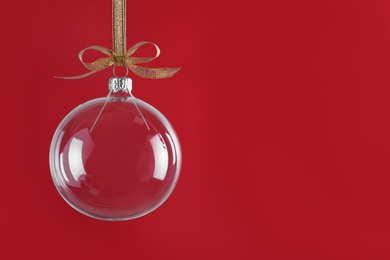 Photo of Transparent glass Christmas ball with golden ribbon and bow against red background. Space for text