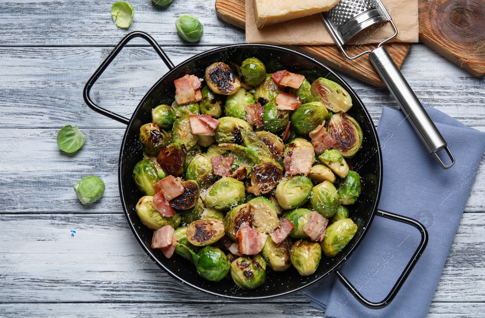 Photo of Delicious Brussels sprouts with bacon in pan on color wooden table, flat lay