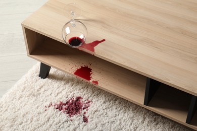 Photo of Overturned glass and spilled red wine on white carpet indoors