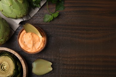 Delicious cooked artichoke with tasty sauce on wooden table, flat lay. Space for text