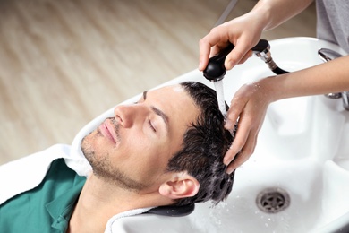 Stylist washing client's hair at sink in beauty salon