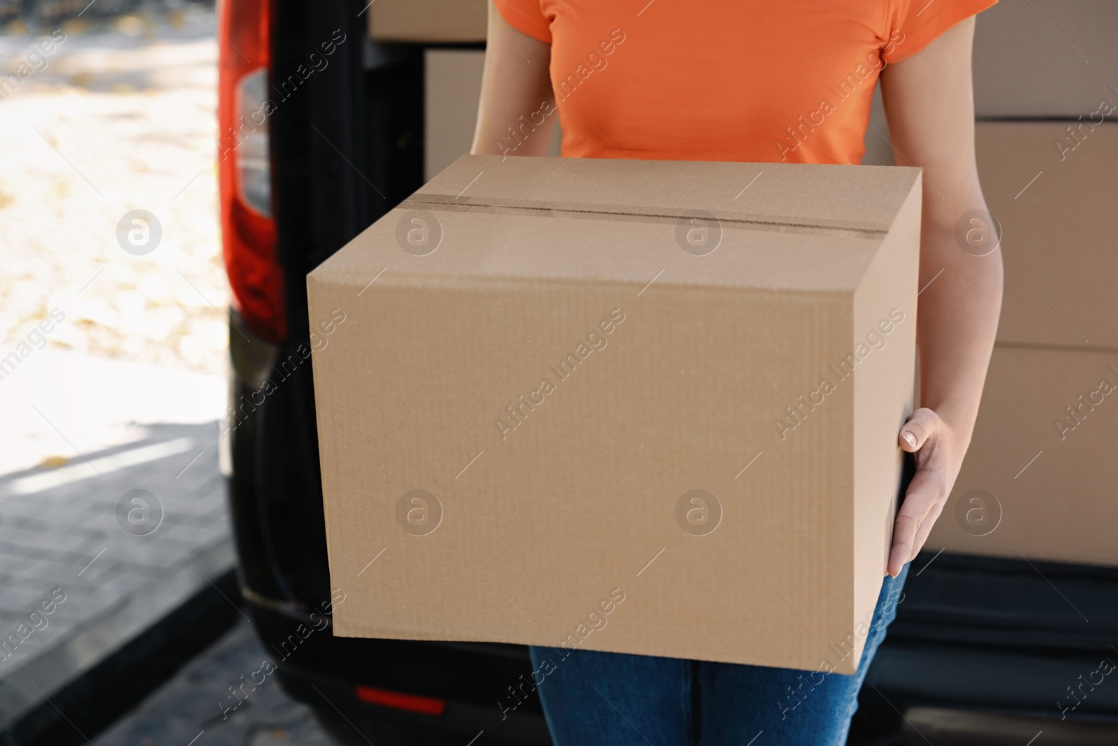 Photo of Courier holding package near delivery truck outdoors, closeup