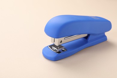 Blue stapler on beige background. Space for text