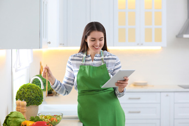 Young woman with apron and tablet in kitchen