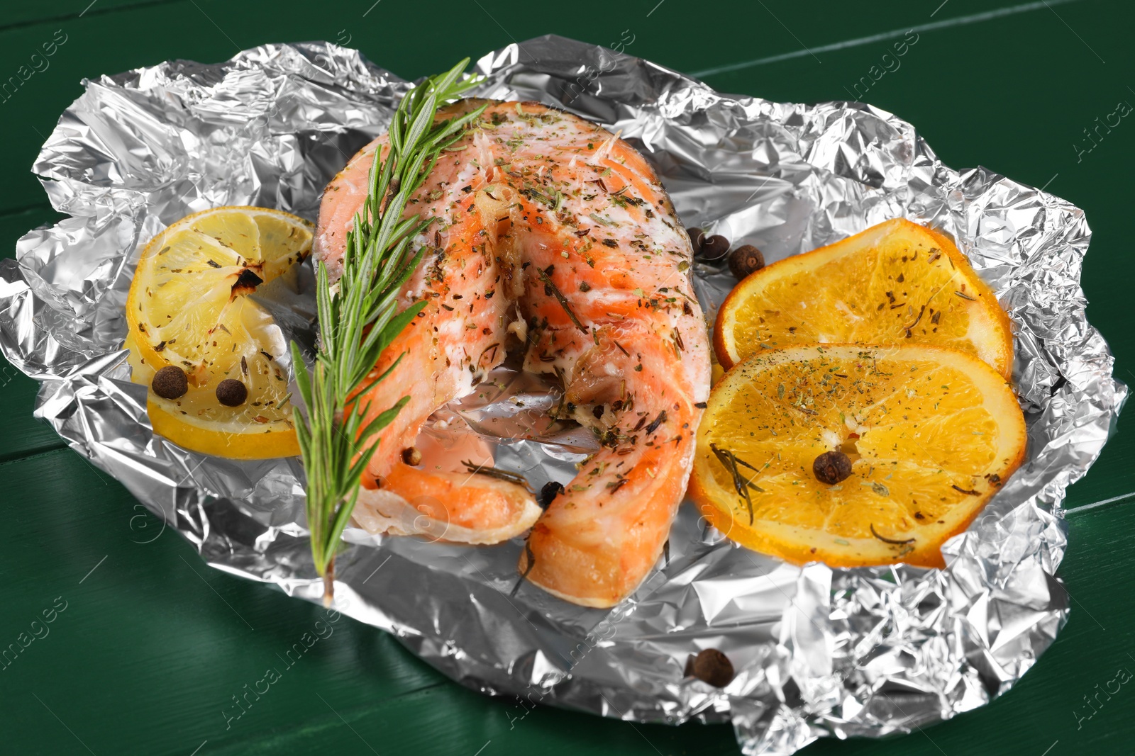Photo of Tasty salmon baked in foil with citrus fruits and rosemary on green wooden table, closeup