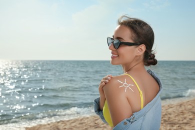 Photo of Beautiful young woman with sun protection cream on shoulder at beach