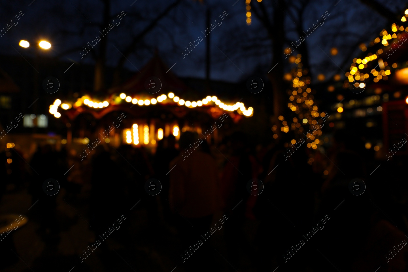 Photo of People walking at Christmas fair, blurred view. Street decorated with festive lights