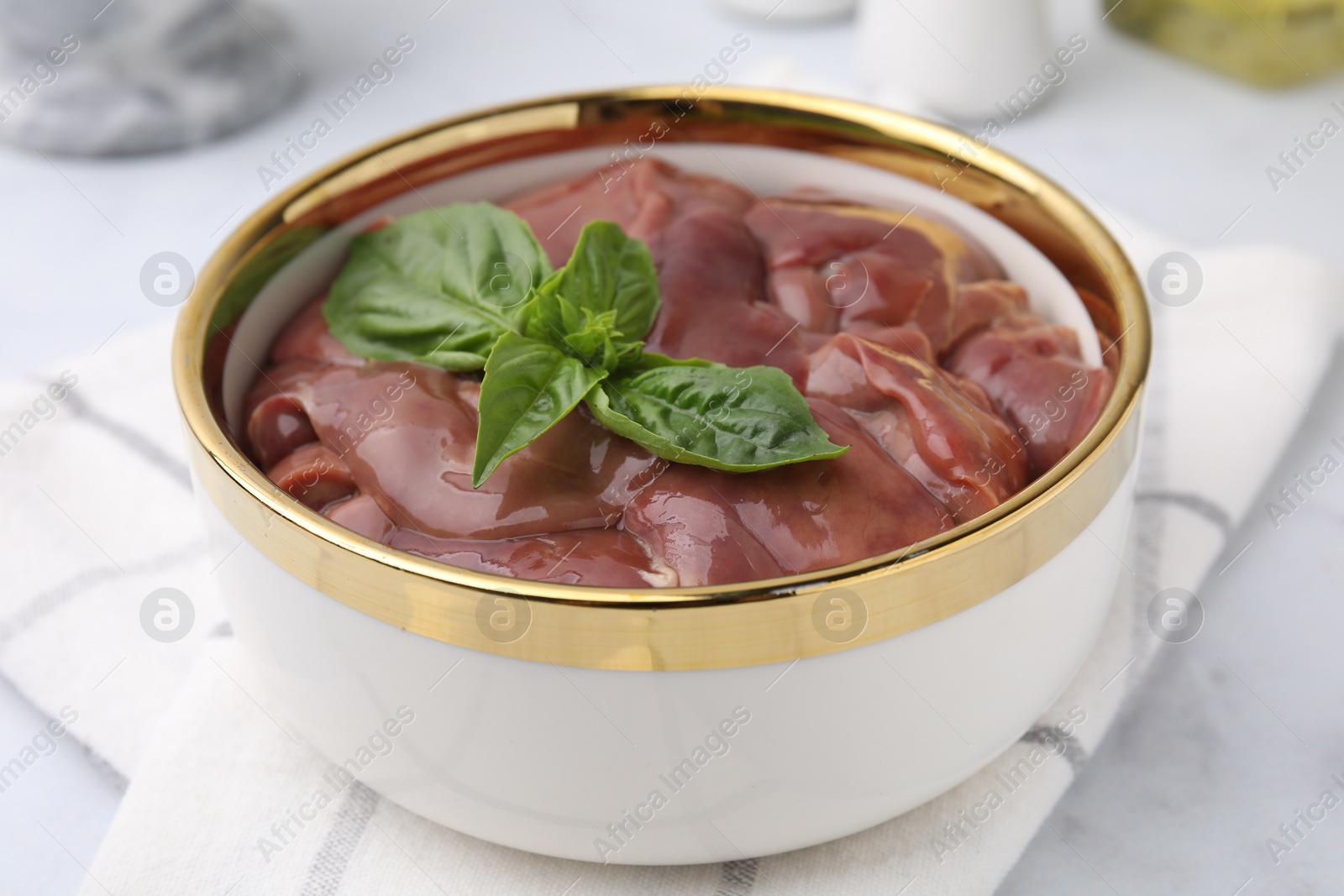 Photo of Bowl with raw chicken liver and basil on white marble table, closeup
