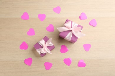 Photo of Beautiful gift boxes and paper hearts on wooden table, flat lay. Valentine's Day celebration