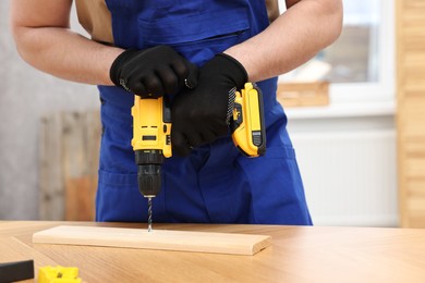 Young worker using electric drill at table in workshop, closeup