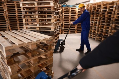Image of Workers moving wooden pallets with manual forklift in warehouse