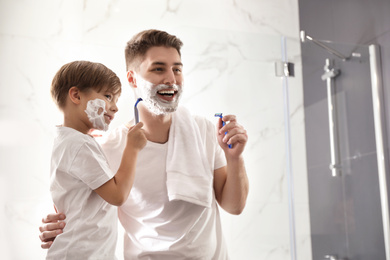 Photo of Dad and son with shaving foam on their faces having fun in bathroom