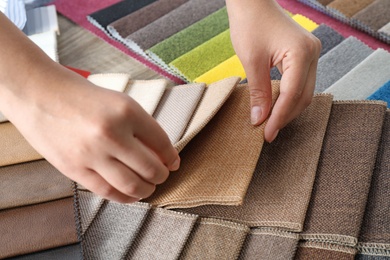 Young woman choosing among upholstery fabric samples, closeup. Interior design