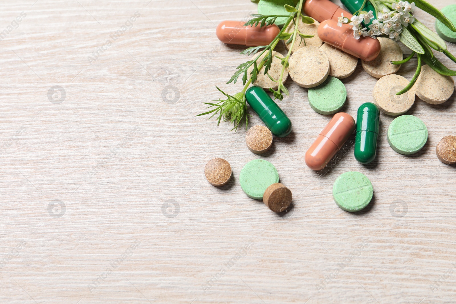 Photo of Different pills and herbs on wooden table, above view with space for text. Dietary supplements