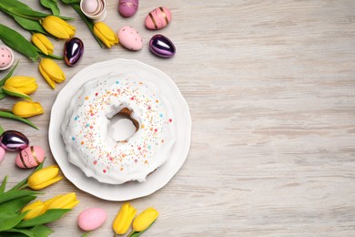 Easter cake with sprinkles, painted eggs and tulips on white wooden table, flat lay. Space for text