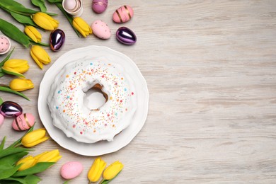 Photo of Easter cake with sprinkles, painted eggs and tulips on white wooden table, flat lay. Space for text