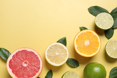 Different cut and whole citrus fruits on yellow table, flat lay. Space for text