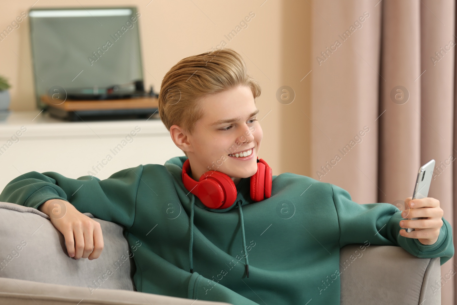 Photo of Teenage boy with headphones using smartphone at home