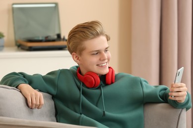 Photo of Teenage boy with headphones using smartphone at home