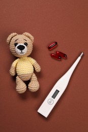 Photo of Toy bear, thermometer and pills on brown background, flat lay