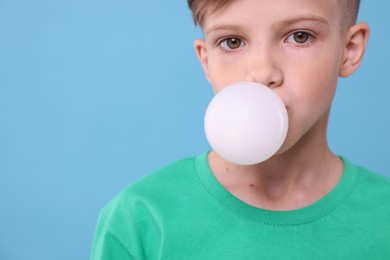 Photo of Boy blowing bubble gum on light blue background, space for text