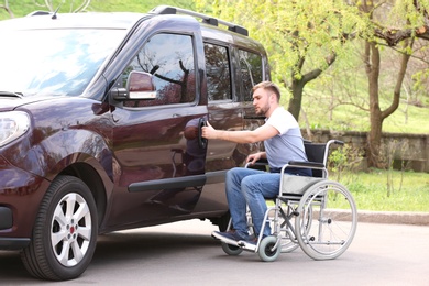 Photo of Young man in wheelchair opening door of his van outdoors