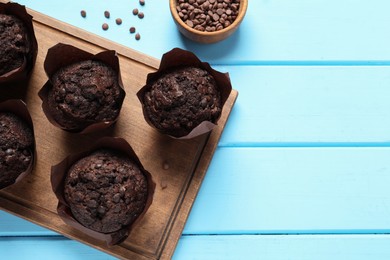 Photo of Tasty chocolate muffins on light blue wooden table, top view. Space for text