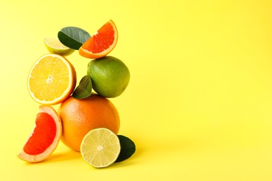 Photo of Fresh ripe citrus fruits and green leaves on yellow background, space for text