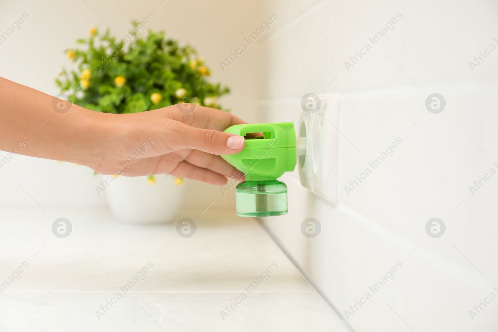Photo of Woman plugging electric vaporizer with insect repellent liquid at home, closeup