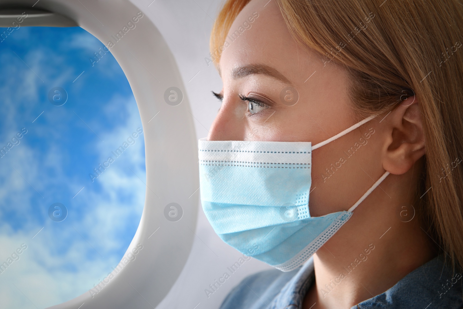 Image of Traveling by airplane during coronavirus pandemic. Woman with face mask near porthole