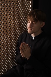 Catholic priest praying near wooden partition in confessional