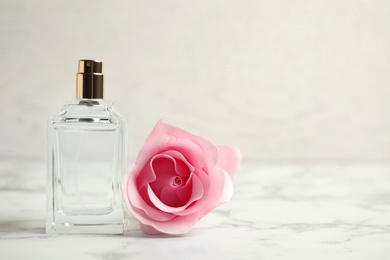 Photo of Bottle of perfume and beautiful rose on white marble table. Space for text