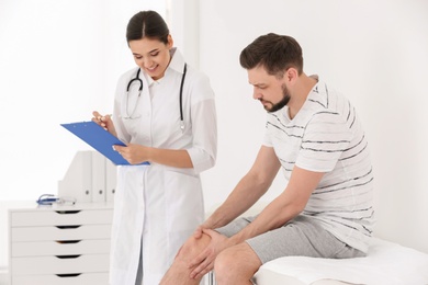 Doctor examining male patient with injured leg in clinic